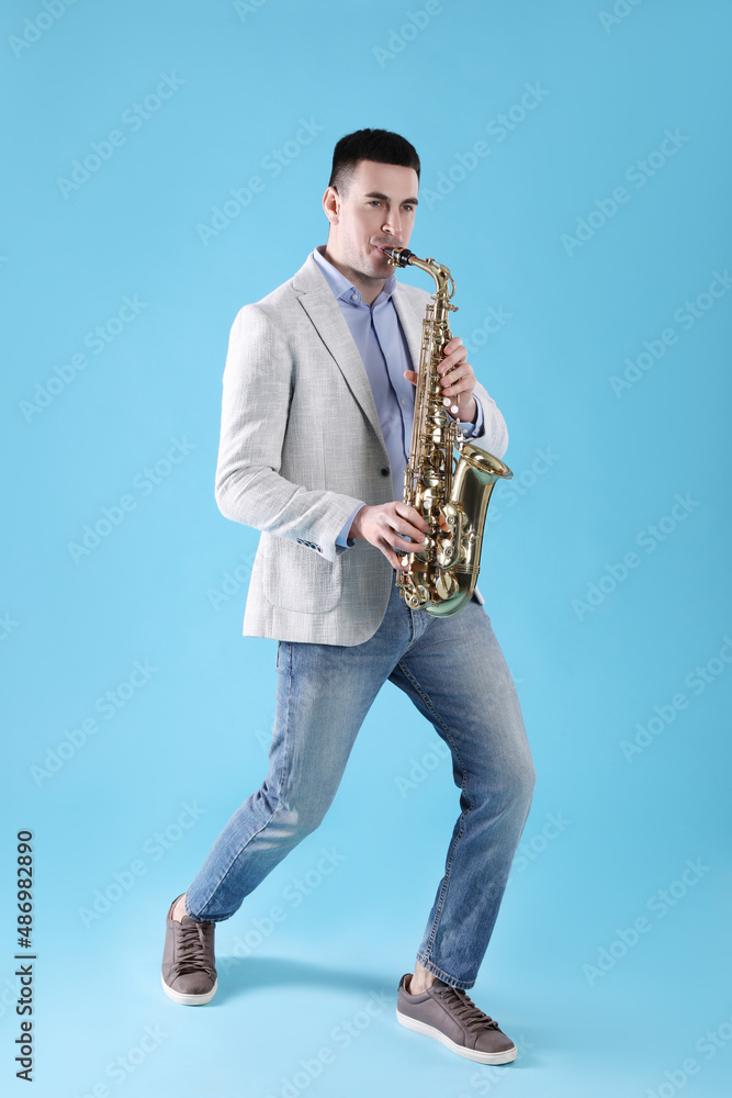 Fototapeta premium Young man playing saxophone on light blue background