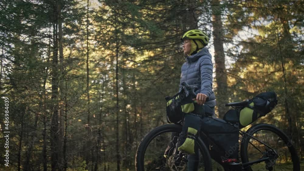 The woman travel on mixed terrain cycle touring with bike bikepacking outdoor. The traveler journey with bicycle bags. Stylish bikepacking, bike, sportswear in green black colors. Magic forest park. The woman travel on mixed terrain cycle touring with bike bikepacking outdoor. The traveler journey with bicycle bags. Stylish bikepacking, bike, sportswear in green black colors. Magic forest park.