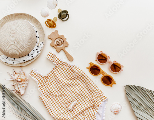 Flat lay Summer kids accessories on brown background. Cute retro swimsuit, straw hat, sunglasses, bib, wooden toys and seashells, summer holiday concept photo