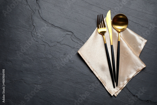 Set of golden cutlery with napkin on black table, top view. Space for text