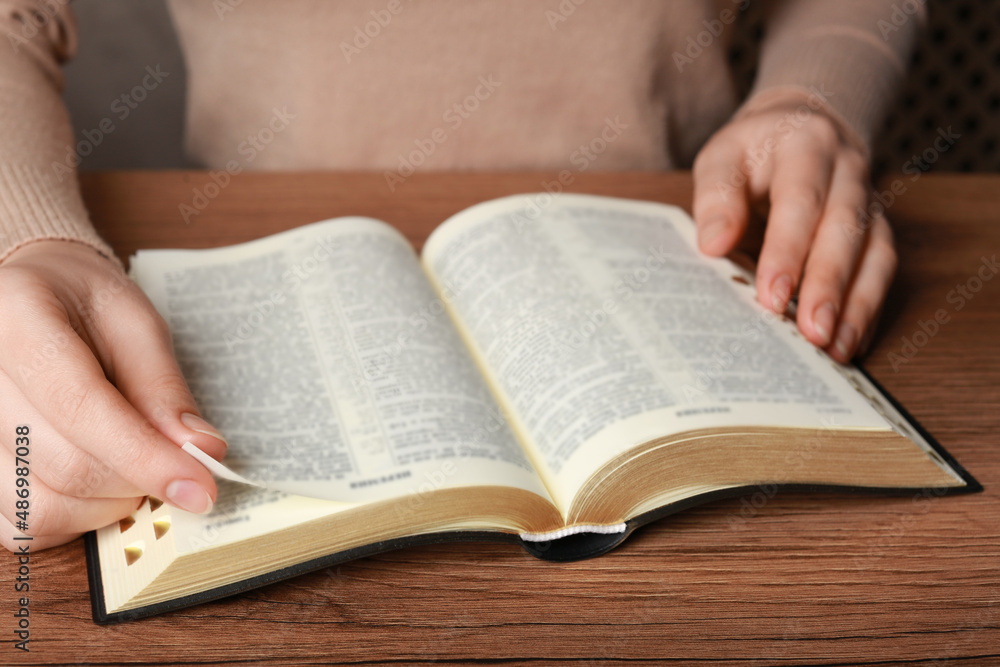 Woman reading Bible at wooden table, closeup Woman reading Bible at wooden table, closeup