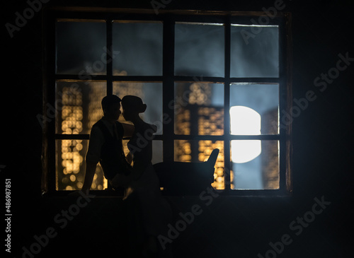 A realistic dollhouse living room with furniture and window at night. Romantic couple sitting on window. Artwork table decoration with handmade realistic dollhouse. Selective focus.