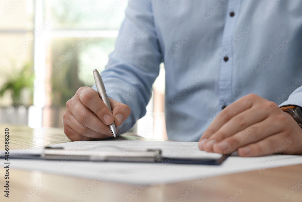 Man signing contract at table in office, closeup. Man signing contract at table in office, closeup.