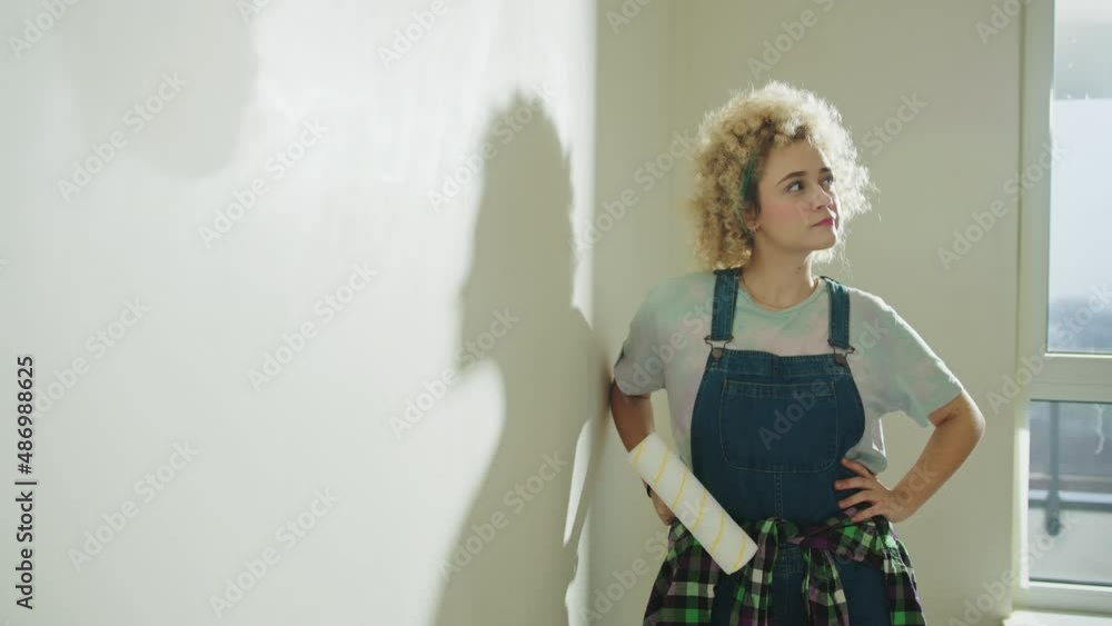 Young girl in dungarees is preparing to paint the walls of home with paint roller Young girl in dungarees is preparing to paint the walls of home with paint roller