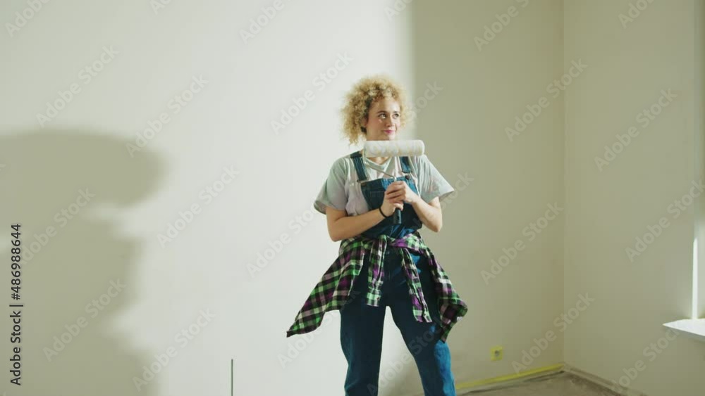 Young satisfied girl makes repairs in the apartment Paint Roller. wall painting concept Young satisfied girl makes repairs in the apartment Paint Roller. wall painting concept