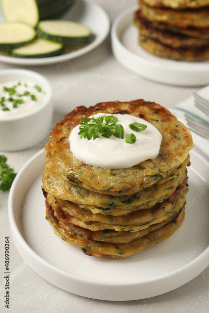 Delicious zucchini pancakes with sour cream served on light grey table Delicious zucchini pancakes with sour cream served on light grey table