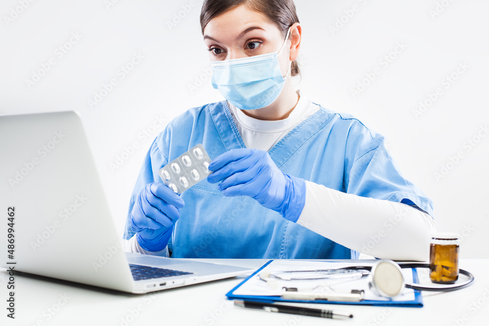 Woman GP doctor holding medicine prescribing patient therapy during online virtual appointment over laptop computer in office Woman GP doctor holding medicine prescribing patient therapy during online virtual appointment over laptop computer in office