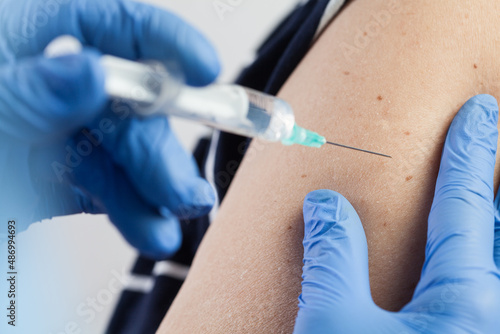 Medical worker injecting vaccine shot to patients shoulder  arm closeup detail