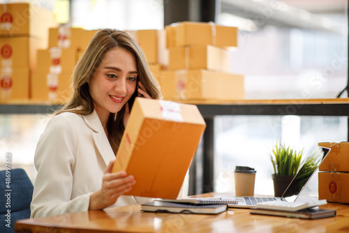  Startup SME small business entrepreneur SME or freelance Asian woman using a laptop with box, Young success Asian woman with her hand lift up, online marketing packaging box and delivery, SME concep