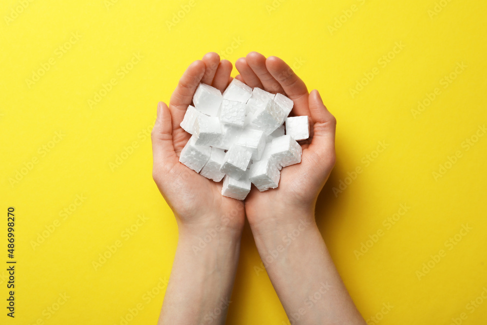 Woman with handful of styrofoam cubes on yellow background, top view Woman with handful of styrofoam cubes on yellow background, top view