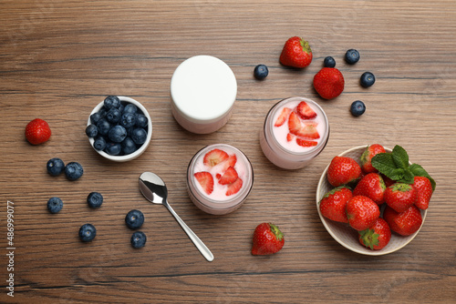 Jars of fresh yogurt, strawberry and blueberry on wooden table, flat lay