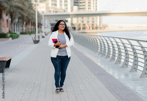 An Indian girl walks along the embankment with books in her hands.
