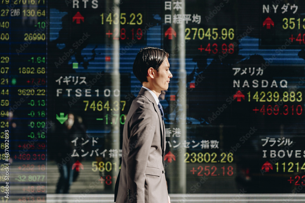 世界の株価ボードの前を通り過ぎる人 世界の株価ボードの前を通り過ぎる人