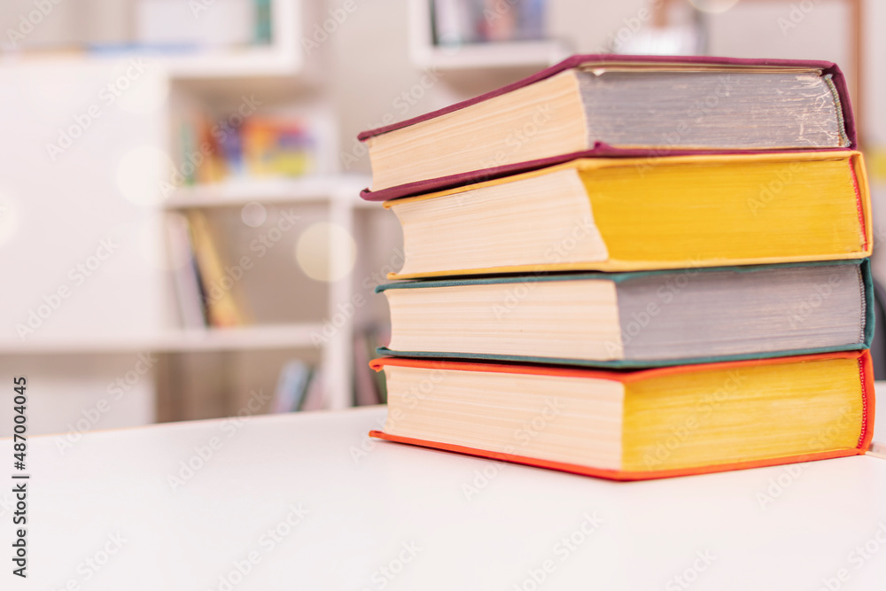 Thick old books with colorful covers lie in pile on white office table against backdrop of bookshelf. Thick old books with colorful covers lie in pile on white office table against backdrop of bookshelf.