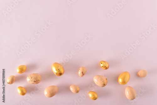 Various Easter eggs of yellow shades lie on a pink background. Easter background with painted eggs and sequins. Copy space. Flat lay, top view.