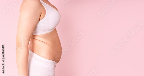 a fat girl holding a hand with excess fat on her stomach on a pink background. the concept of a woman's lifestyle with a diet to reduce the belly. recovery after childbirth. place for text