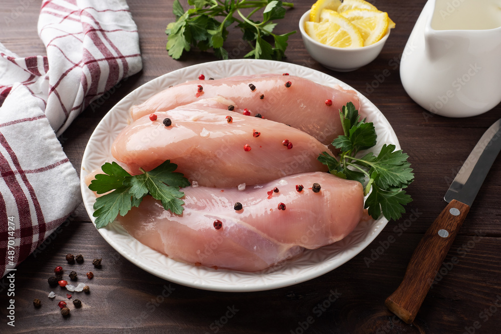 Raw chicken breast fillet on a plate, dark wooden background. Raw chicken breast fillet on a plate, dark wooden background.