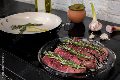 Fresh pieces of meat lie on a wooden board with sprigs of rosemary and garlic. Nearby is a bottle of olive oil. Delicious grilled meat for lunch or dinner. For the keto diet.