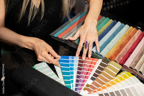 A woman examines and selects fabric samples in the catalog for decorating the interior, her new sofa, curtains, pillows. Reviews wall paint color palette