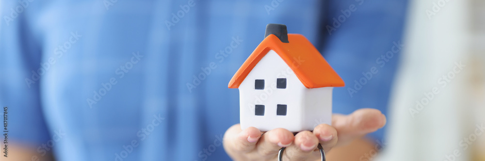 Female hand holding toy house and metal keys closeup Female hand holding toy house and metal keys closeup