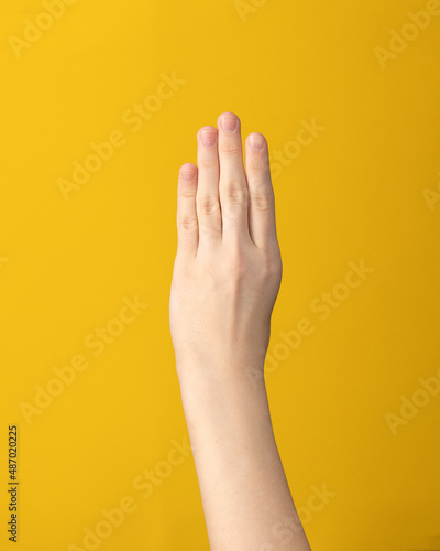 Female hand isolated showing four fingers index, middle, ring and little on yellow background.