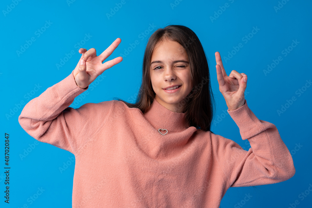 Young teen girl showing a peace symbol with fingers against blue background Young teen girl showing a peace symbol with fingers against blue background