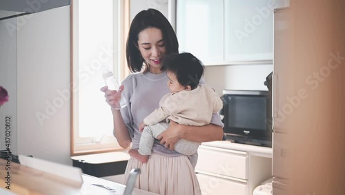 赤ちゃんを抱っこしながら粉ミルクを作るお母さん photo