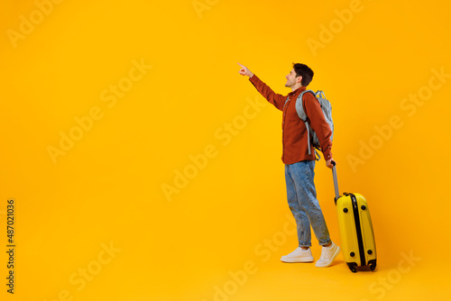 Tourist Man Pointing Finger Aside Standing With Suitcase  Yellow Background
