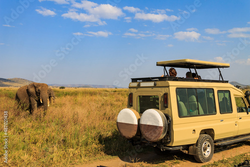 Tourists in SUV car watching and taking photos of african elephants in Serengeti national park, Tanzania. African safari