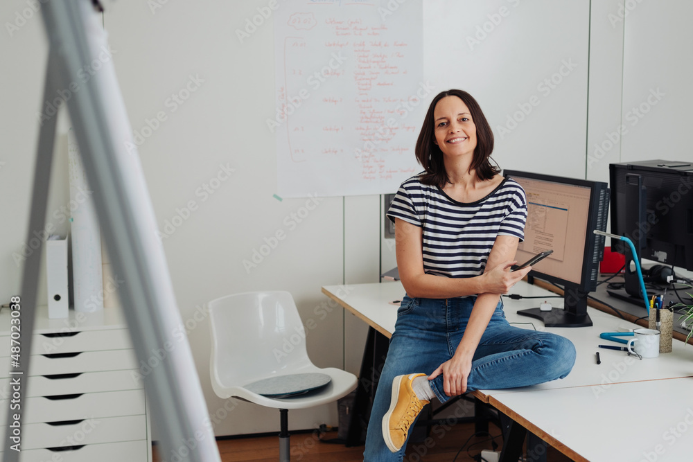 Happy relaxed businesswoman perched on her desk