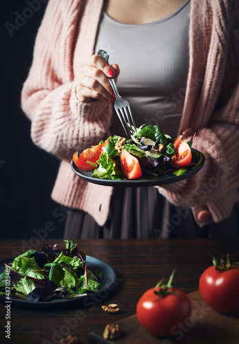 Woman eating tomato and letuce salad with walnuts. Moody image of unrecognizable woman eating salad.