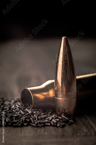 Macro shot of a cartridge case, bullet and gunpowder on a wooden background with limited depth of field, vertical photo, soft focus