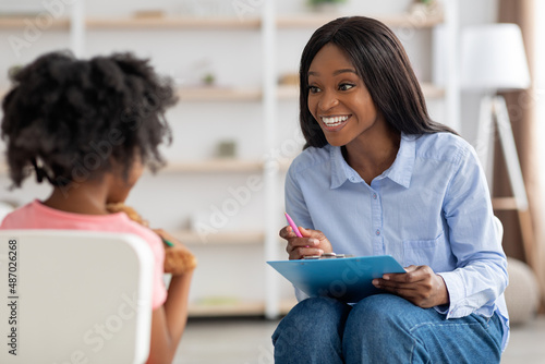 Smiling pretty black woman child development specialist talking to girl