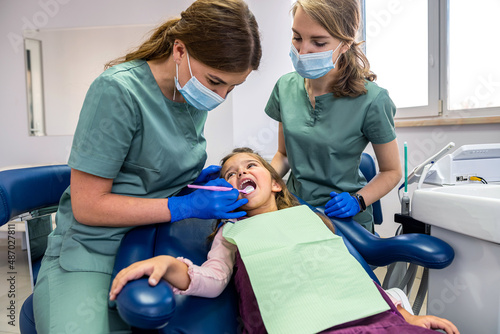Beautiful female dentist with her assistant in medical uniform looking at children s teeth.