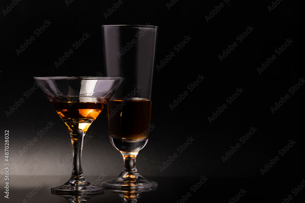 Two glass glasses on a beautiful leg with an alcoholic drink on a black background.