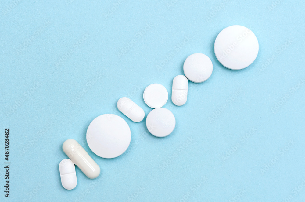 Various white health pills and on a blue background. The concept of medicine, pharmacy and healthcare.