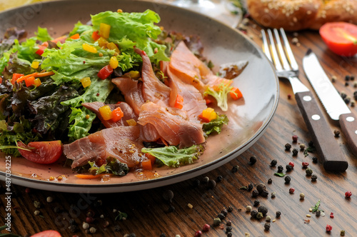 fresh salad with tuna, tomatoes and corn in a flat round plate with cutlery on the table 