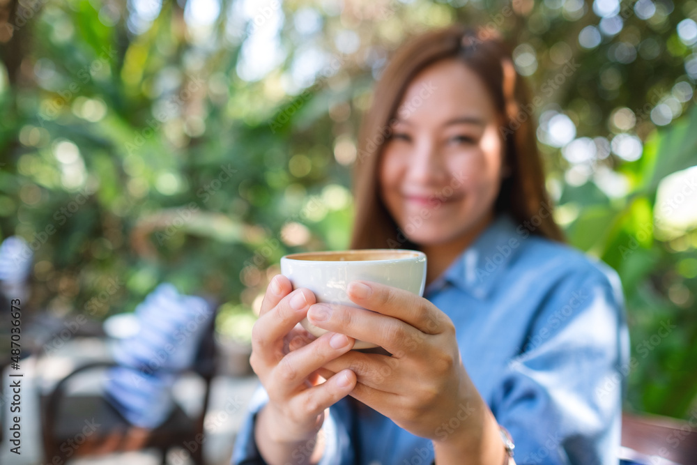 Blurred of a young woman holding and drinking hot coffee in the outdoors cafe Blurred of a young woman holding and drinking hot coffee in the outdoors cafe