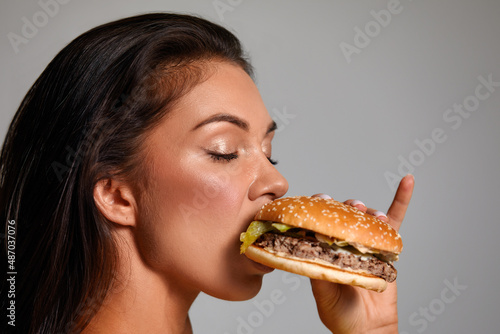 cheat meal concept. athlete woman is posing with fast food on light gray background  studio shot. young sporty woman is holding fast food close up.