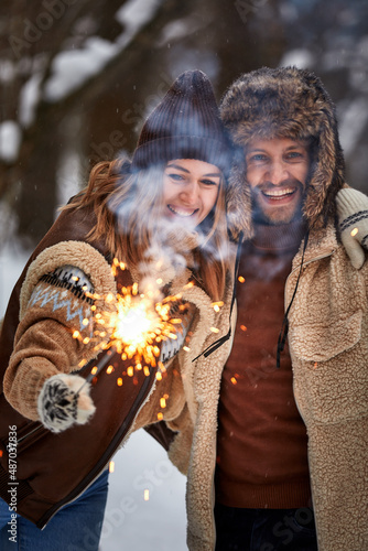 Selective focus. Couple Love Story in Snow Forest Kissing and Holding Sparklers. Couple in Winter Nature. Couple Celebrating. Valentine's day date.