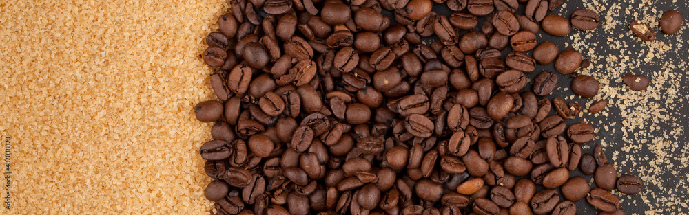 Scattered coffee beans and brown sugar on a black countertop.