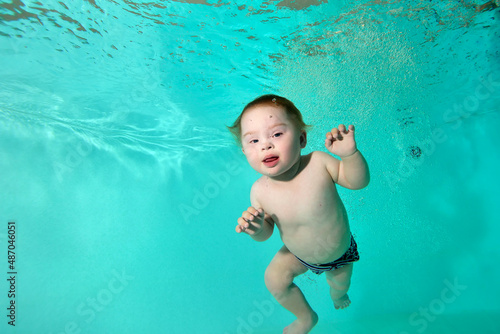 Portrait of a happy disabled child with Down syndrome who swims and plays underwater in a turquoise water pool. Close-up. Horizontal orientation.