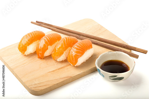 Sushi, salmon, and chopsticks are put on a wooden chopping board There is a sauce cup on the side. isolated on white background.