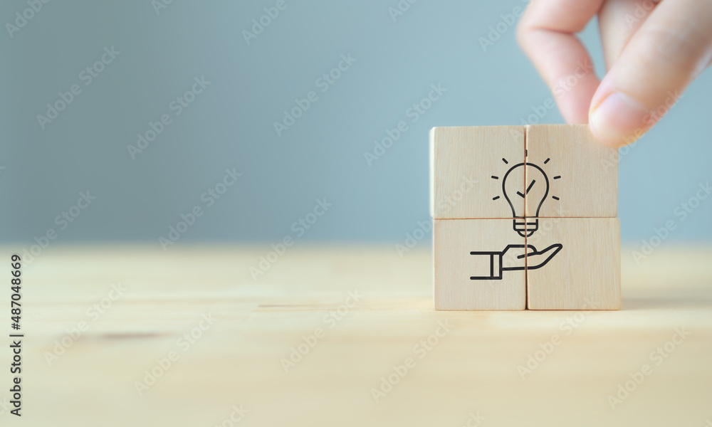 New idea, solution, suggestion concept.  Hand puts the wooden cubes with light bulb on hand icon on beuatiful grey background and copy space. Business review, strategy suggestion for business growth. - obrazy, fototapety, plakaty 