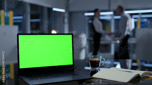 Focus on laptop with green screen on desk in office. Business people shaking hands  photo