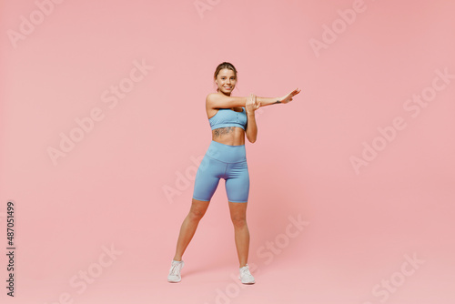 Full sizeyoung sporty fitness trainer instructor woman wear blue tracksuit spend time in home gym train do stretch lunge exercise rise hands up isolated on plain pink background Workout sport concept
