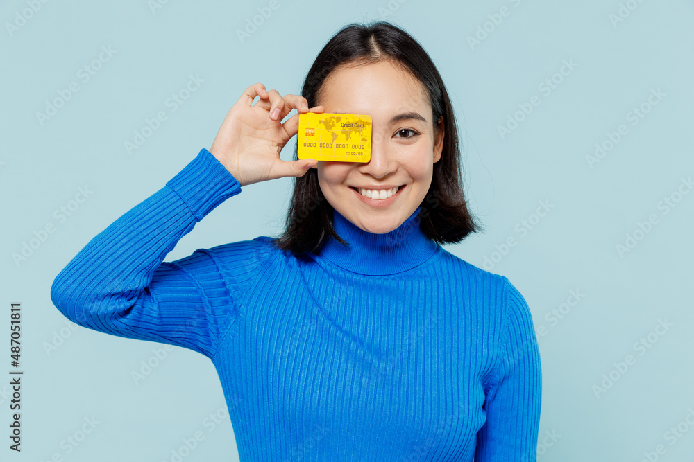 Fascinating fun joyful young woman of Asian ethnicity 20s years old wear blue shirt hold in hand credit bank card cover close hiding eye isolated on plain pastel light blue background studio portrait Fascinating fun joyful young woman of Asian ethnicity 20s years old wear blue shirt hold in hand credit bank card cover close hiding eye isolated on plain pastel light blue background studio portrait
