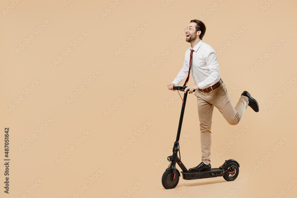 Full body side view young successful employee business man corporate lawyer in white shirt red tie glasses work in office riding electric e scooter isolated on plain beige background studio portrait Full body side view young successful employee business man corporate lawyer in white shirt red tie glasses work in office riding electric e scooter isolated on plain beige background studio portrait