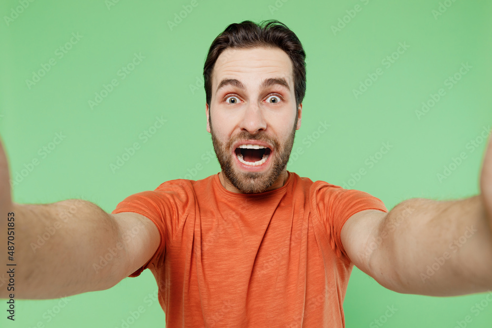 Close up young shocked surprised fun cool happyman 20s in casual orange t-shirt doing selfie shot pov on mobile phone isolated on plain pastel light green background studio. People lifestyle concept Close up young shocked surprised fun cool happyman 20s in casual orange t-shirt doing selfie shot pov on mobile phone isolated on plain pastel light green background studio. People lifestyle concept