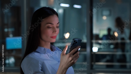 Side view of successful businesswoman use mobile phone standing near window in office